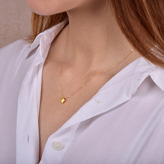 Gold necklace with a small pendant worn by a person in a white shirt.