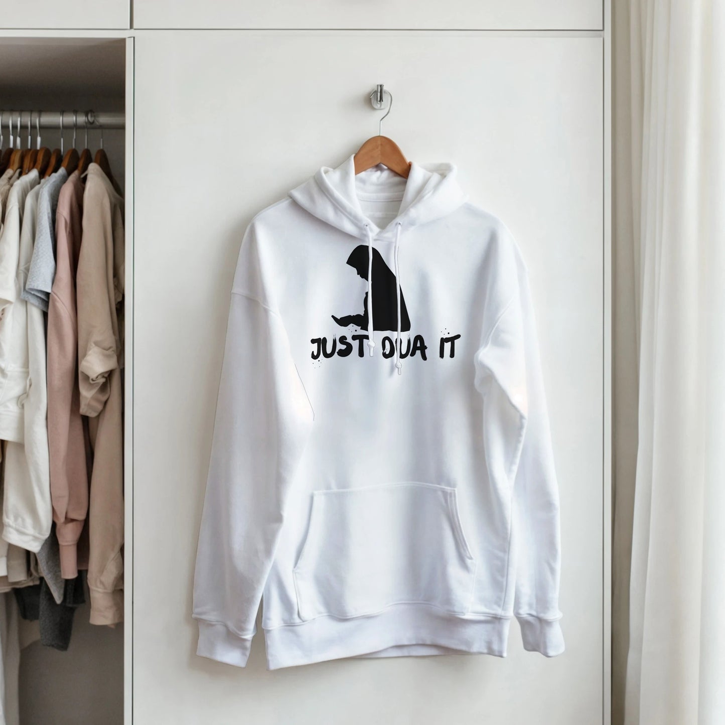 Unisex white pullover hoodie with black graphic and text hanging on wooden hanger in wardrobe