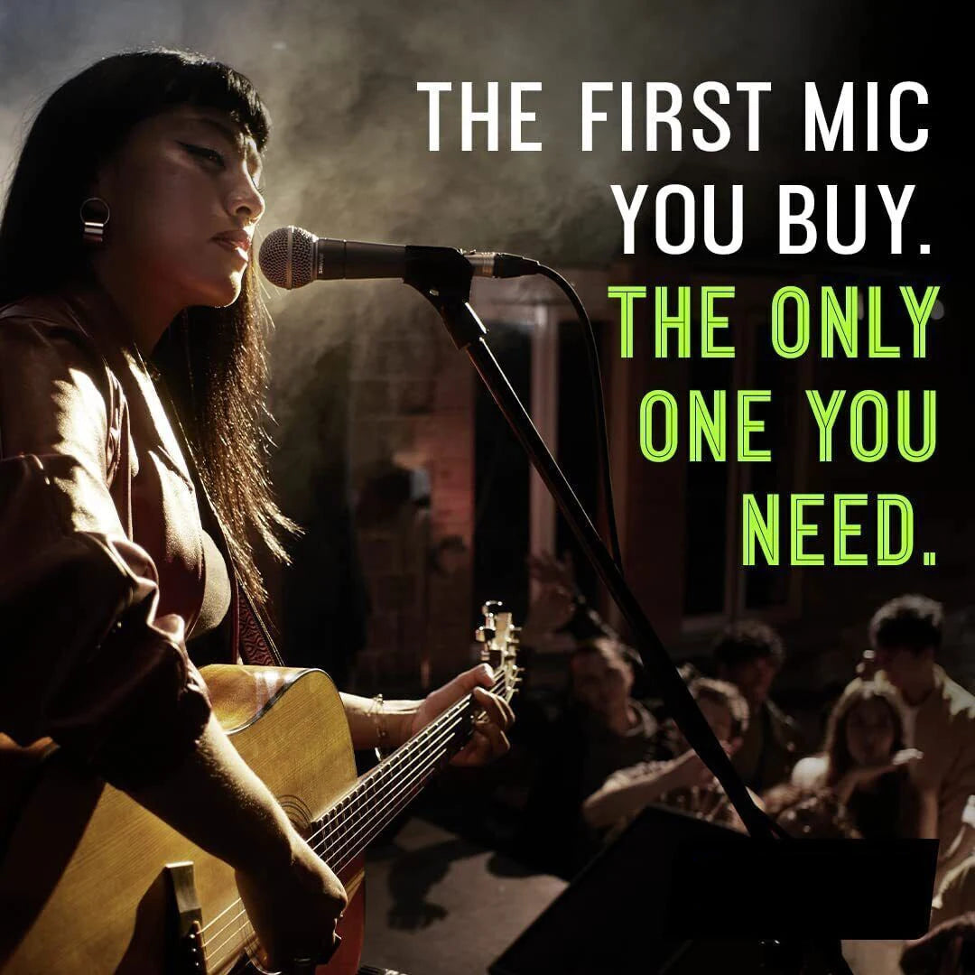 Female singer playing acoustic guitar on stage singing into SM58 dynamic vocal microphone with seated audience and stage lighting