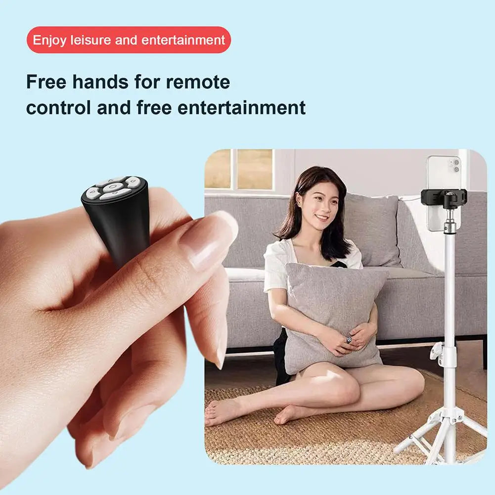 Bluetooth ring remote control black held between fingers with woman taking hands free smartphone selfie on tripod
