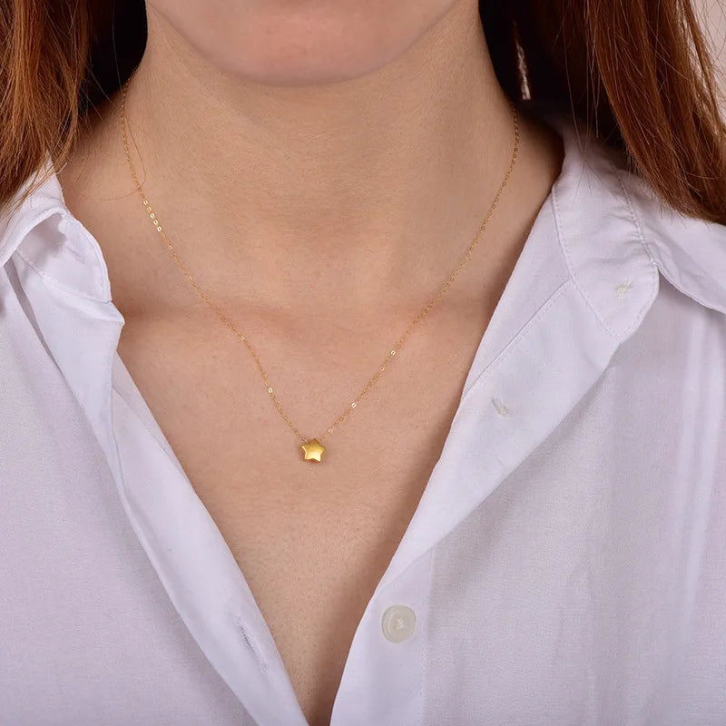 Person wearing a gold necklace with a star pendant on a white shirt.