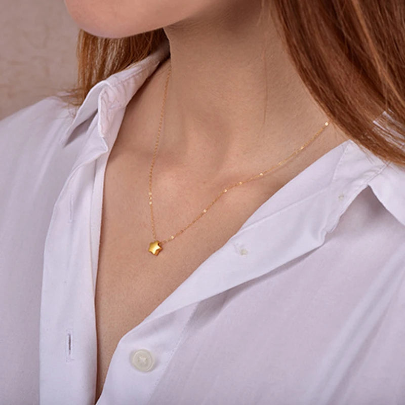 Gold necklace with a small pendant worn by a person in a white shirt.
