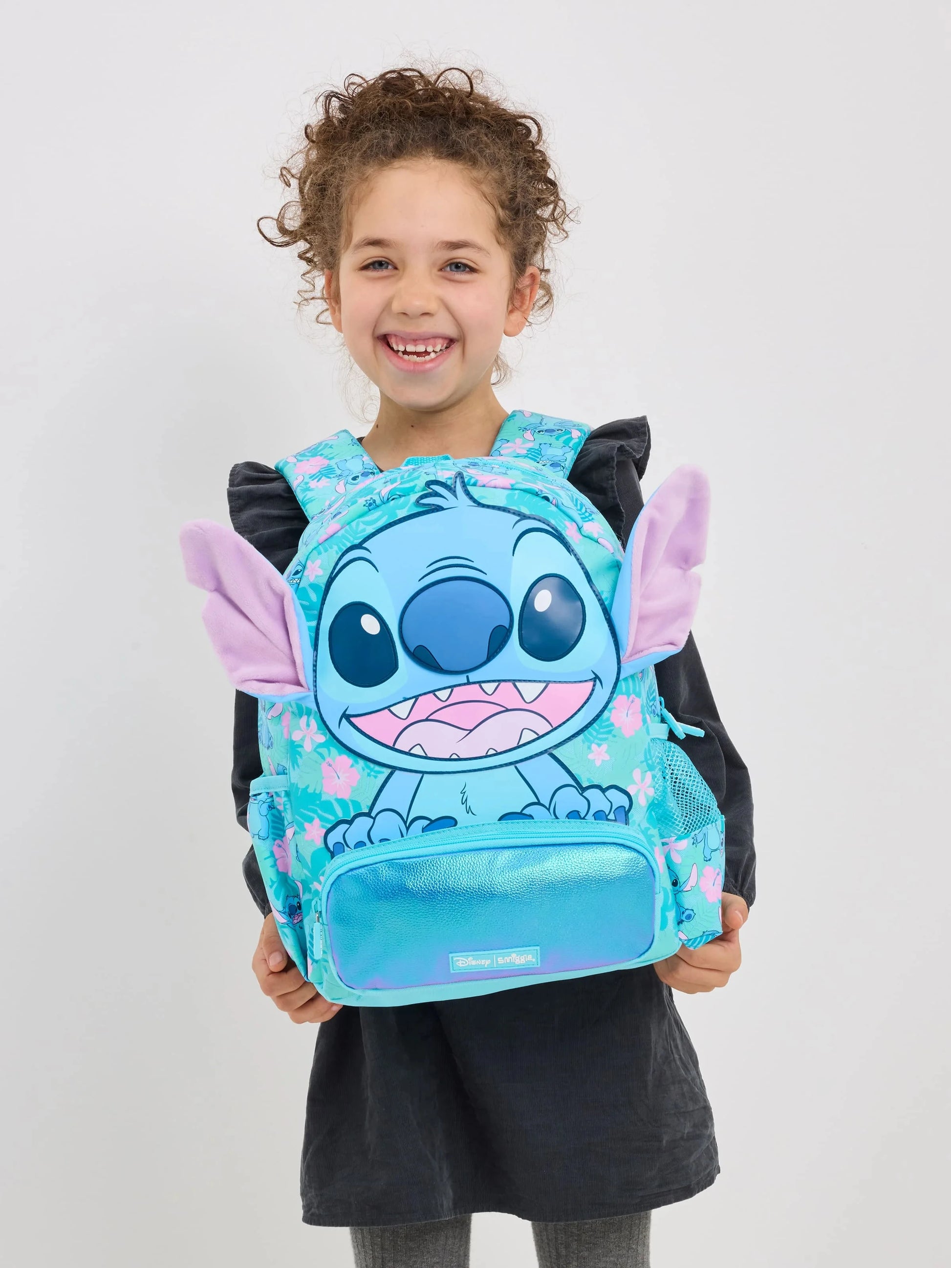 Smiling girl wearing a turquoise character backpack with plush ears Smiggle school bag set for girls.