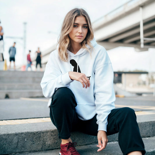 Woman wearing a unisex white pullover hoodie sitting outdoors on a concrete step near urban bridge