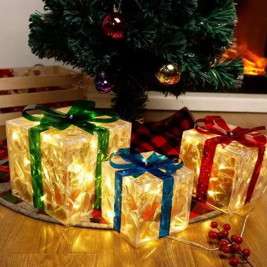 Set of LED Christmas box ornaments in clear with ribbons, glowing under a Christmas tree